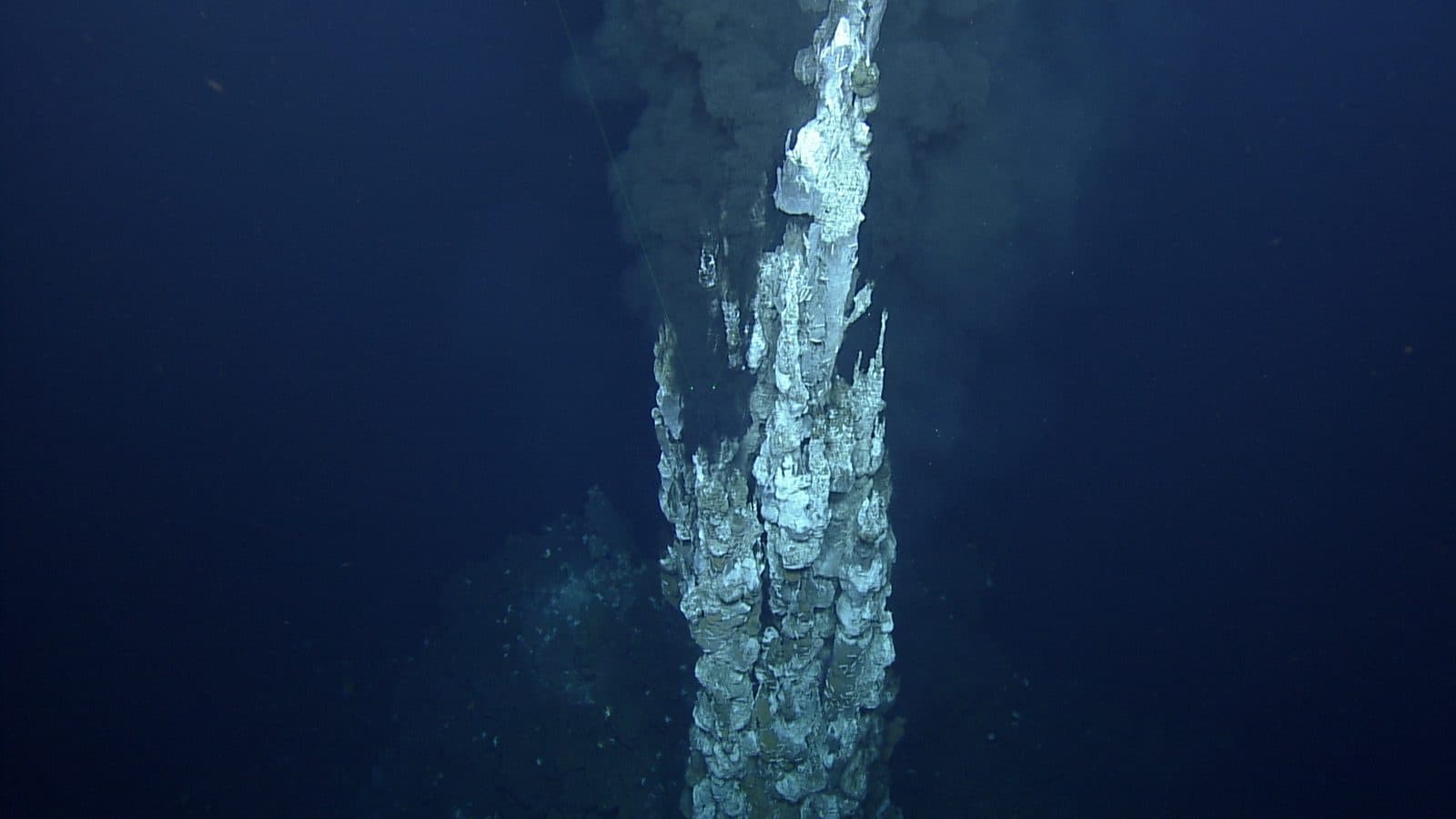 A tall pale hydrothermal chimney rising from the seafloor into dark blue water