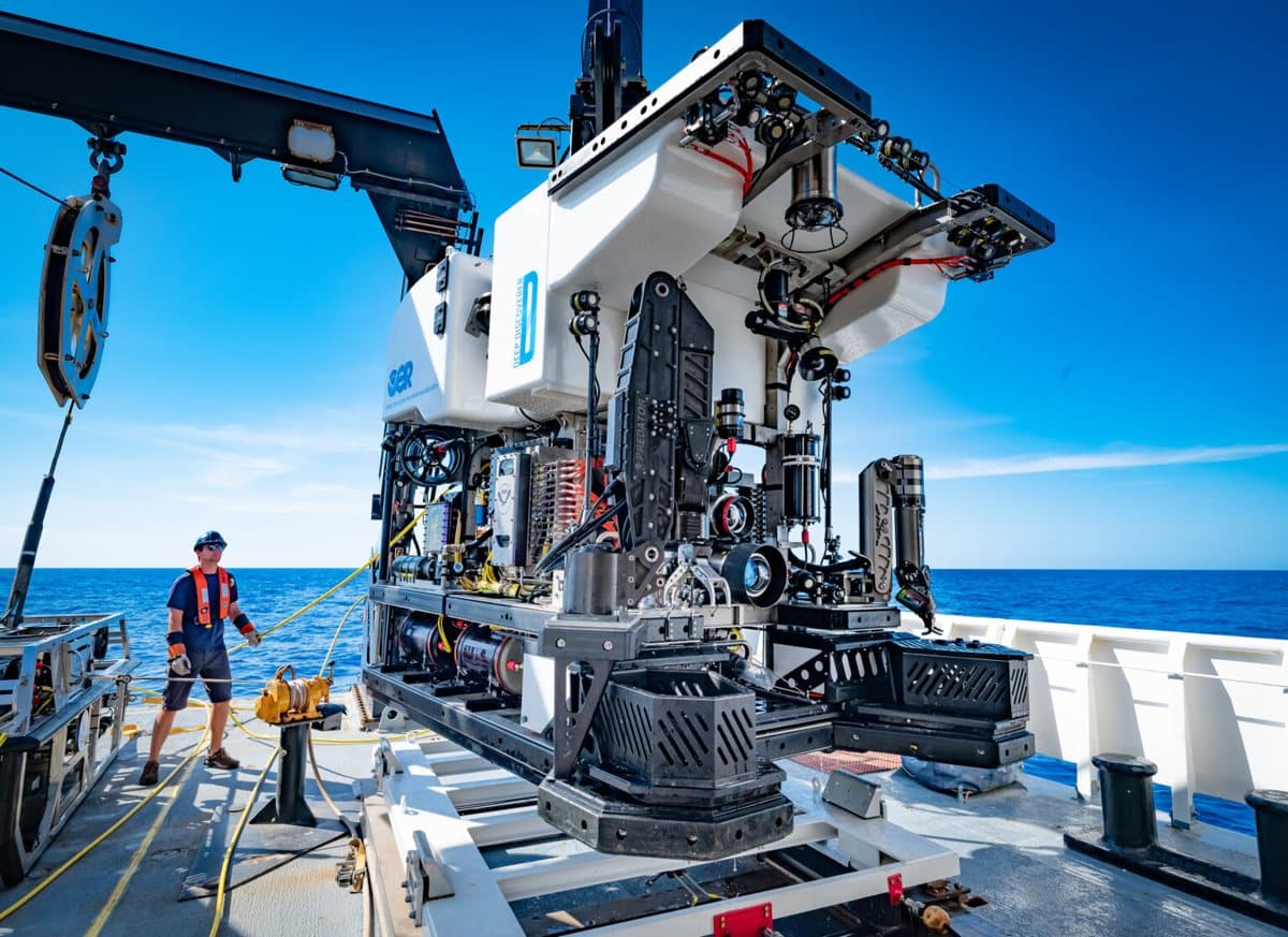 A large work-class remotely operated vehicle on a ship's aft deck, a technician handling its tether before launch